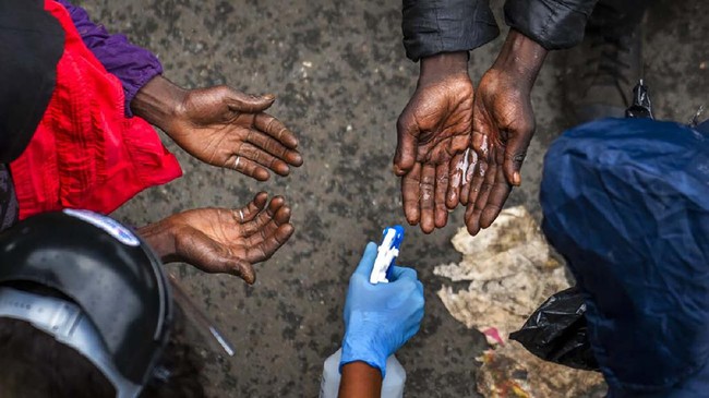 Homeless people waiting to receive food baskets from private donors, get their hands sanitized Monday, April 13, 2020 downtown Johannesburg. Because of South Africa's imposed lockdown to contain the spread of COVID-19, many are not able to work. The new coronavirus causes mild or moderate symptoms for most people, but for some, especially older adults and people with existing health problems, it can cause more severe illness or death.(AP Photo/Jerome Delay)