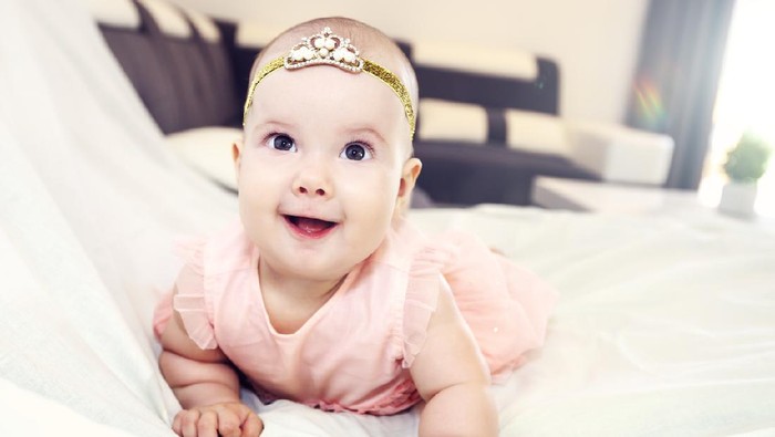 Charming beautiful lovely small female baby with plump cheeks creeps on bed, looks innocently on something, being naughty. Cute baby infant plays alone. Newborn kid crawls. Enthusiastic child