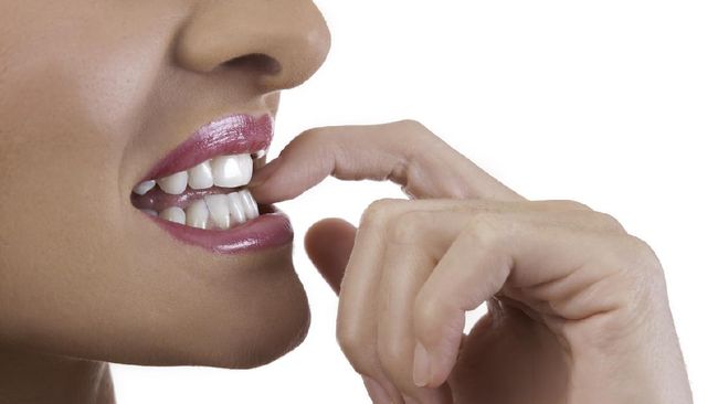 Beautiful young woman bites her nails. Sha has perfect skin and white teeth, isolated on a white background.