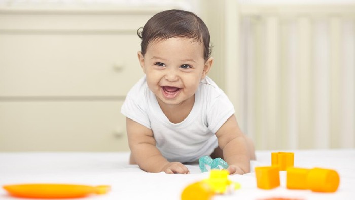 Charming beautiful lovely small female baby with plump cheeks creeps on bed, looks innocently on something, being naughty. Cute baby infant plays alone. Newborn kid crawls. Enthusiastic child