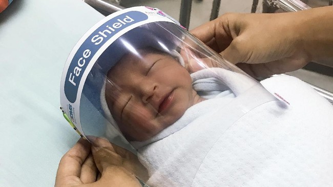 In this Friday, April 3, 2020, photo released by Paolo Hospital Samutprakarn, a nurse adjusts tiny face shield for a newborn baby to protect from new coronavirus at the newborn nursery of the hospital in Samutprakarn province, central Thailand. The new coronavirus causes mild or moderate symptoms for most people, but for some, especially older adults and people with existing health problems, it can cause more severe illness or death. (Paolo Hospital Samutprakarn via AP)