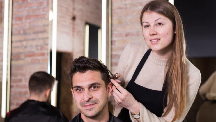 Young skillful woman barber making hairstyle for male client in hair studio