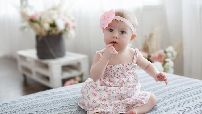 Charming beautiful lovely small female baby with plump cheeks creeps on bed, looks innocently on something, being naughty. Cute baby infant plays alone. Newborn kid crawls. Enthusiastic child