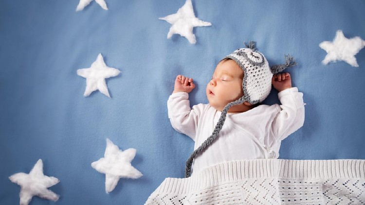 Cute newborn baby girl lying in the bed. 2 month old child in owl hat sleeping on blue blanket with stars