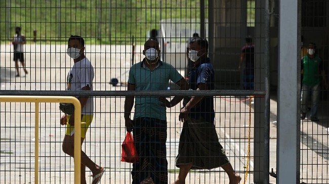 Foreign workers, wearing face masks as a preventive measure against the spread of the COVID-19 novel coronavirus, looks out from a fence of the workers' dormitory in Singapore on April 9, 2020. - Migrant workers in Singapore are living in fear following a surge of coronavirus infections in their dormitories where they say cramped and filthy conditions make social distancing impossible. (Photo by Roslan RAHMAN / AFP) / TO GO WITH Health-virus-Singapore-migration, FOCUS by Catherine Lai and Sam Reeves