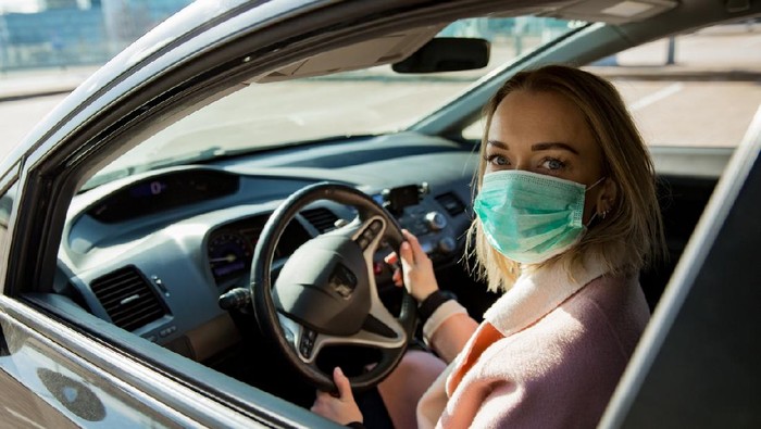 Woman in protective mask driving a car on road. Safe traveling.