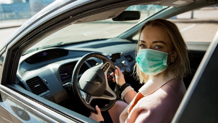 Woman in protective mask driving a car on road. Safe traveling.