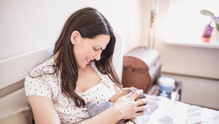 A Japanese mother breastfeeding her baby girl in a home nursery.