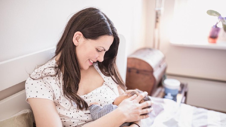 A Japanese mother breastfeeding her baby girl in a home nursery.