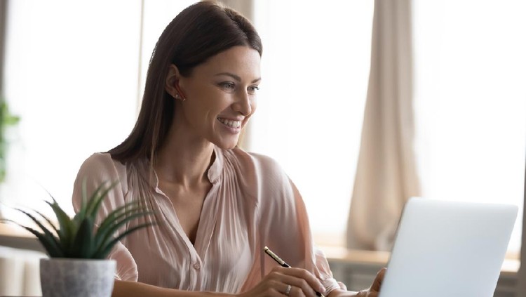 kecantikan Smiling young woman wearing headphones sit at desk working at laptop making notes, happy millennial female in modern earphones study watch webinar on computer handwrite in notebook