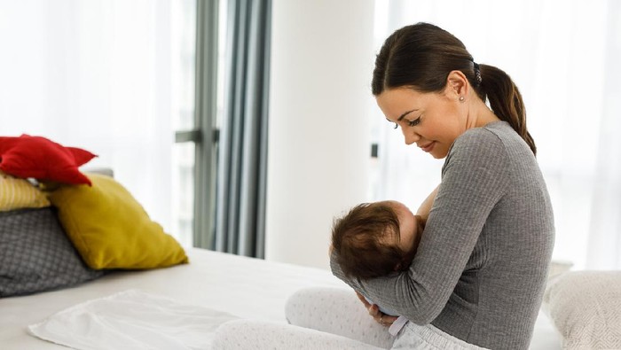 A Japanese mother breastfeeding her baby girl in a home nursery.