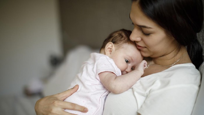 A Japanese mother breastfeeding her baby girl in a home nursery.