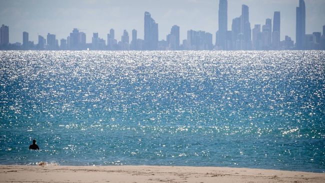 A lone swimmer is seen at Coolangatta Beach with Surfers Paradise in the background, on the Queensland - New South Wales border in Brisbane on April 15, 2020. - A state border that bisects Australia's neighbouring beachside towns of Coolangatta and Tweed Heads has rarely troubled locals, long accustomed to crossing the invisible line daily for coffee or a surf. But as Australia began shutting down last month in response to the coronavirus outbreak, Queensland closed its border to slow the virus spread from worst-hit New South Wales (NSW) state -- for the first time since the Spanish Flu pandemic a century ago. (Photo by Patrick HAMILTON / AFP)