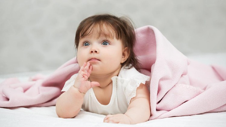 Portrait of baby girl lying on blanket indoors