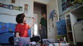 Keseharian Seorang Dokter Covid-19 di Italia Dr. Giovanni Passeri peeks from the open door of the room of his son Francesco, playing with Lego, to say hello to him after coming back from a night shift in the COVID-19 section of the Maggiore Hospital in Parma, northern Italy Thursday, April 9, 2020. Passeri takes all precautions to avoid unintentionally passing the virus on to his wife or his 10-year-old son when he comes home. He sleeps in the garret of his apartment and keeps safe distance from them at all times. (AP Photo/Domenico Stinellis)