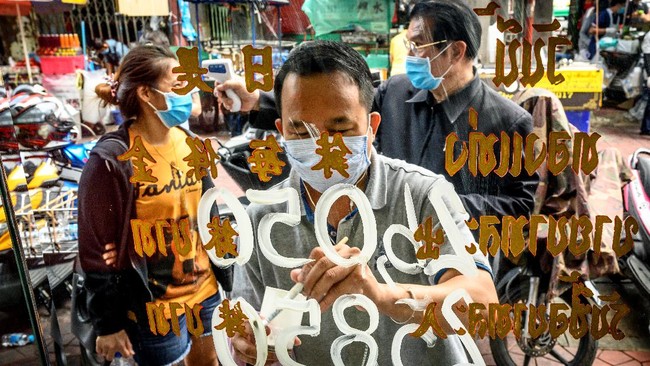 An employee wearing a face mask amid fears of the spread of COVID-19 coronavirus paints the new prices of gold on the shop window of a goldsmith as another employee checks the temperature of a customer in Bangkok's Chinatown on April 15, 2020. - Hundreds of Bangkok residents rushed to goldsmith shops in order to sell their jewelries as gold prices reached its highest levels since 2012. (Photo by Mladen ANTONOV / AFP)