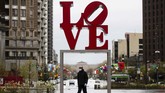 Nyalang Edisi 18 April 2020 A person wearing a protective face mask and gloves as a precaution against the coronavirus walks by the Robert Indiana sculpture