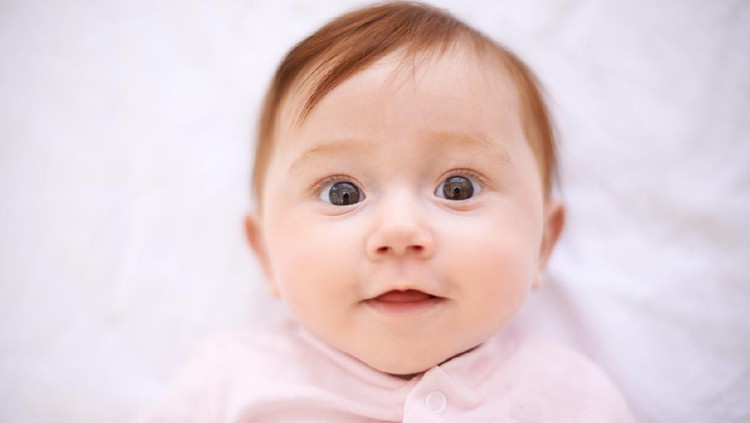 Portrait of baby girl lying on blanket indoors