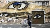 Nyalang edisi 18 April 2020 A couple wearing face masks and pushing a pram walks past a mural in the Trastevere district of Rome on April 13, 2020 during the country's lockdown aimed at curbing the spread of the COVID-19 infection, caused by the novel coronavirus. (Photo by Vincenzo PINTO / AFP)