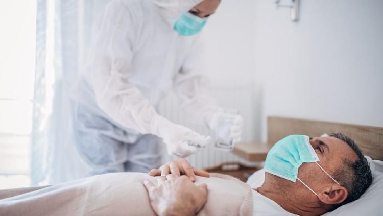 Man and woman, senior man lying in hospital bed because of coronavirus infection, female doctor is giving medicine to a patient.