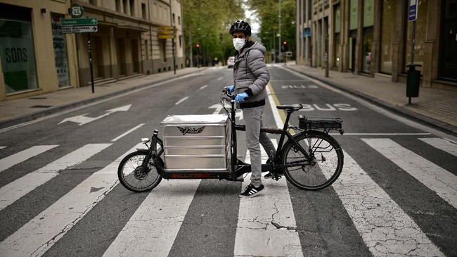 In this Thursday, April 16, 2020 photo, Sidi Hasan psses for a photograph with his delivery bicycle in Pamplona, northern Spain. As Spain hunkers down after five weeks of home confinement, there are the brave few who keep the country going during a coronavirus outbreak that has killed over 20,000 of their fellow citizens. These laborers_ butchers, taxi drivers, pharmacists_ in the northern city of Pamplona as well as the rest of Spain's cities and towns are unified by their courage and one piece of equipment: the face mask. (AP Photo/Alvaro Barrientos)