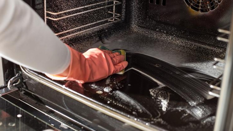 Close up of female hands with protective gloves scrubbing oven in kitchen