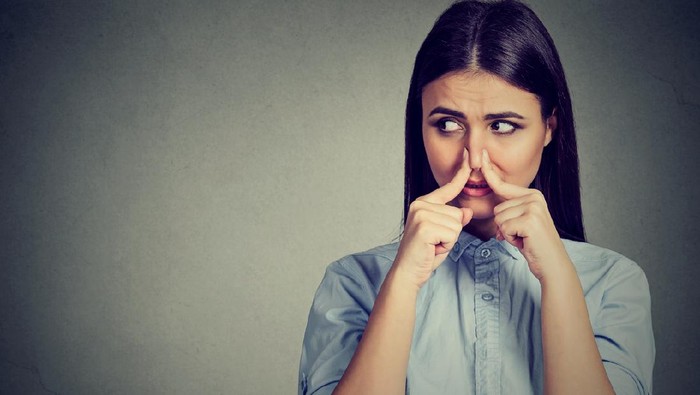Woman pinches nose with fingers looks with disgust away something stinks bad smell isolated on gray background.