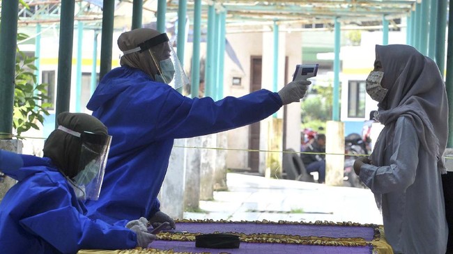 Petugas kesehatan yang dilengkapi dengan Alat Pelindung Diri (APD) memeriksa suhu salah satu penumpang yang turun di terminal Alang Alang Lebar  Palembang,Sumsel, Senin(20/4/2020).  Dengan ditetapkannya Palembang sebagai zona merah, Pemerintah Kota Palembang menyiagakan tenaga kesehatan dan dinas perhubungan untuk memantau bis dan penumpang yang melintas di Terminal setempat untuk menhantisipasi penyebaran wabah ke luar dan dalam kota,. ANTARA FOTO/Feny Selly/hp.