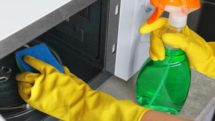 Close up of female hands with protective gloves scrubbing oven in kitchen