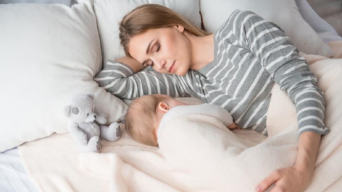 Beautiful mom lying at the back of the baby while the infant is sleeping on the white bed. Asian mother looking at the baby which is her child with love and care.