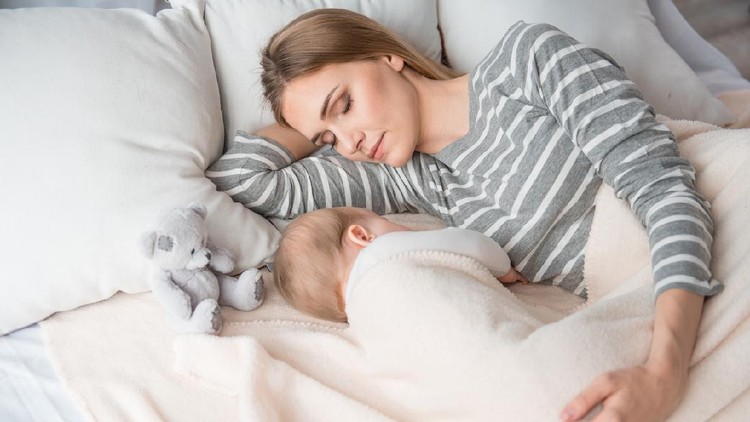 Beautiful mom lying at the back of the baby while the infant is sleeping on the white bed. Asian mother looking at the baby which is her child with love and care.