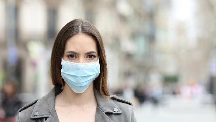 Front view portrait of serious woman with protective mask avoiding contagion looking at camera on street