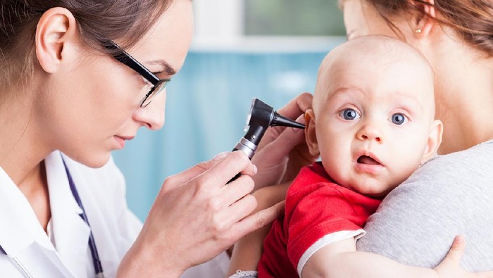 Young doctor examining baby boy with otoscope