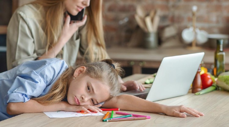 Boredom. Upset girl suffering from mom indifference, laying on kitchen table, mom working with laptop, panorama, free space, cropped