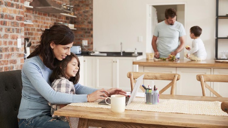 Busy Family Home With Mother Working As Father Prepares Meal