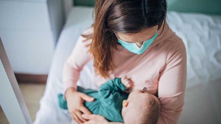 menyusui Two people, mother with protective mask breastfeeding her baby son at home, they are at home do to pandemic outbreak quarantine.