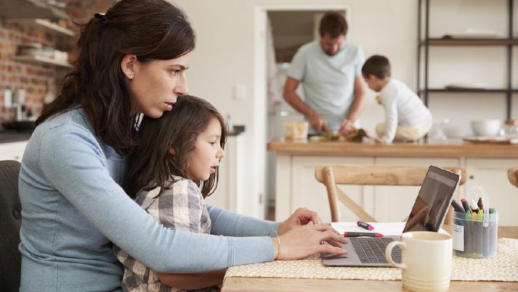 Busy Family Home With Mother Working As Father Prepares Meal