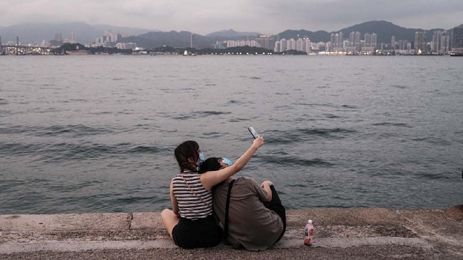A couple wearing face masks, as a precautionary measure against the COVID-19 coronavirus, take a selfie on a cargo dock dubbed Instagram Pier in Hong Kong on April 21, 2020. - Hong Kong has reduced growth of confirmed COVID-19 cases to single digits in recent days, but city authorities say they are not taking any risks. Chief executive Carrie Lam said social distancing measures and some business restrictions would continue for another two weeks until at least May 7. (Photo by Anthony WALLACE / AFP)