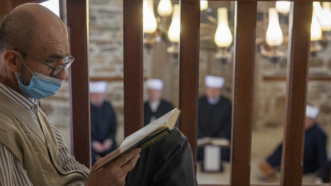 A man reads the Quran as imams attend the Ramadan prayer at a mosque empty of faithful due to social distancing guidelines during the coronavirus outbreak in Zenica, central Bosnia, Thursday, April 23, 2020. The COVID-19 virus pandemic is cutting off the world's Muslims from their cherished Ramadan traditions. (AP Photo/Almir Alic)