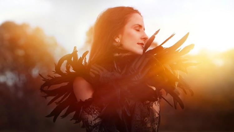 Beautiful Goth woman wearing black lace and feathers in autumn woods