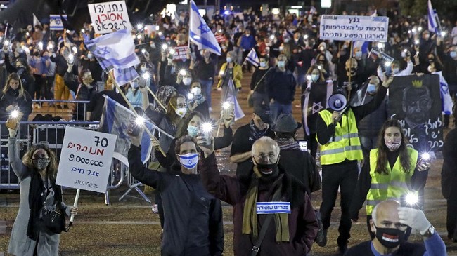 Israelis wearing protective masks lift placards as they take part in a demonstration on April 25, 2020, in Rabin Square in the coastal city of Tel Aviv, to protest what they consider threats to Israeli democracy, against the backdrop of negotiations between Prime Minister Benjamin Netanyahu and his ex-rival Benny Gantz. - The protesters stood two meters apart from each other, thereby respecting the social distancing measures in force to fight the COVID-19 pandemic. (Photo by JACK GUEZ / AFP)