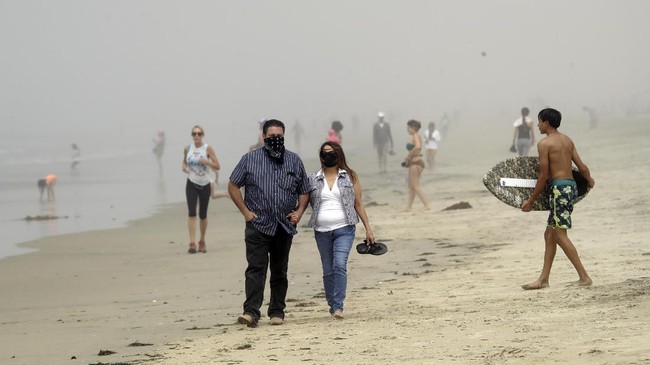 People wear masks as they walk on the beach Sunday, April 26, 2020, in Huntington Beach, Calif. A lingering heat wave lured people to California beaches, rivers and trails again Sunday, prompting warnings from officials that defiance of stay-at-home orders could reverse progress and bring the coronavirus surging back. (AP Photo/Marcio Jose Sanchez)