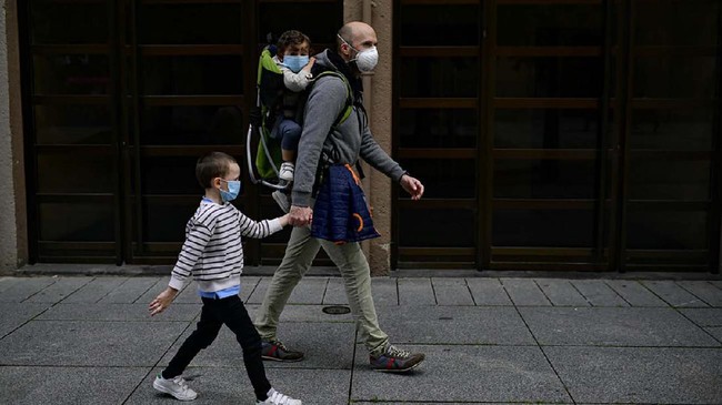 A father with his children wearing face mask to prevent the coronavirus go for a walk at Carlos III promenade, in Pamplona, northern Spain, Sunday, April 27, 2020. On Sunday, children under 14 years old will be allowed to take walks with a parent for up to one hour and within one kilometer from home, ending six weeks of compete seclusion. (AP Photo/Alvaro Barrientos)