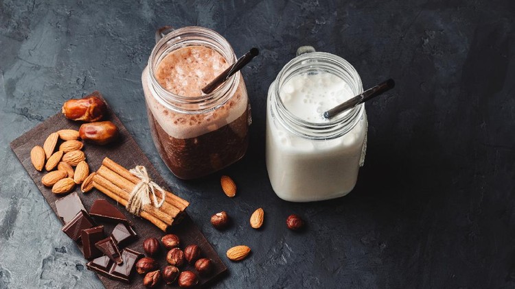 Banana and chocolate smoothie in two jars, protein milkshake, nuts, chocolate cubes, dates, cinnamon sticks, healthy eating on a dark background.
