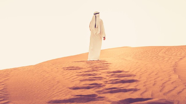 Arab walking on the sand dunes of Dubai and looking at the bright sunlight.