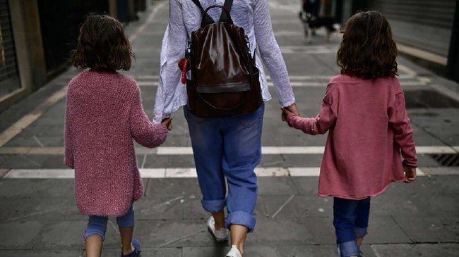 A family go for a walk taking their hands along a street of the old city, in Pamplona, northern Spain, Sunday, April 27, 2020. On Sunday, children under 14 years old will be allowed to take walks with a parent for up to one hour and within one kilometer from home, ending six weeks of compete seclusion. (AP Photo/Alvaro Barrientos)