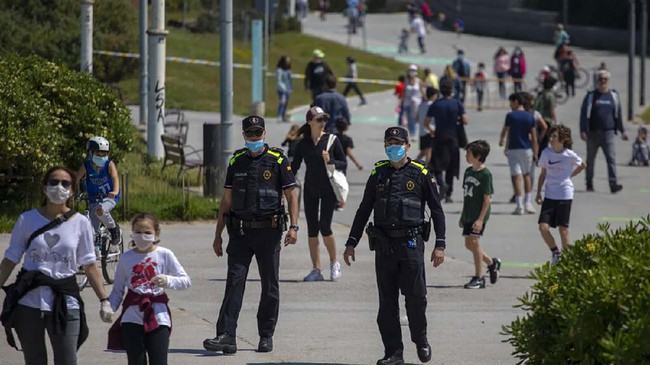 Catalan police officers patrol as families with their children walk along a boulevard in Barcelona, Spain, Sunday, April 26, 2020 as the lockdown to combat the spread of coronavirus continues. On Sunday, children under 14 years old will be allowed to take walks with a parent for up to one hour and within one kilometer from home, ending six weeks of compete seclusion. (AP Photo/Emilio Morenatti)