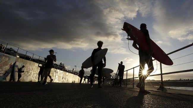 A sign indicates the beach is closed as a surfers arrives for the 7A.M. opening of Bondi Beach in Sydney, Tuesday, April 28, 2020, as coronavirus pandemic restrictions are eased. The beach is open to swimmers and surfers to exercise only. (AP Photo/Rick Rycroft)