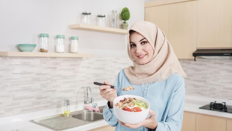 portrait of beautiful young woman wearing hijab with a bowl of granola with fresh fruit for breakfast