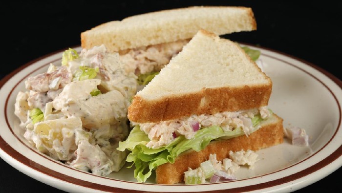 An extreme close up horizontal photograph of a tuna sandwich with potato salad on a white plate. Isolated on black.